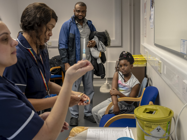 Michael Nnagbo (centro) ve la preparación de la vacuna contra el sarampión para su hija en Wolverhampton, Inglaterra.